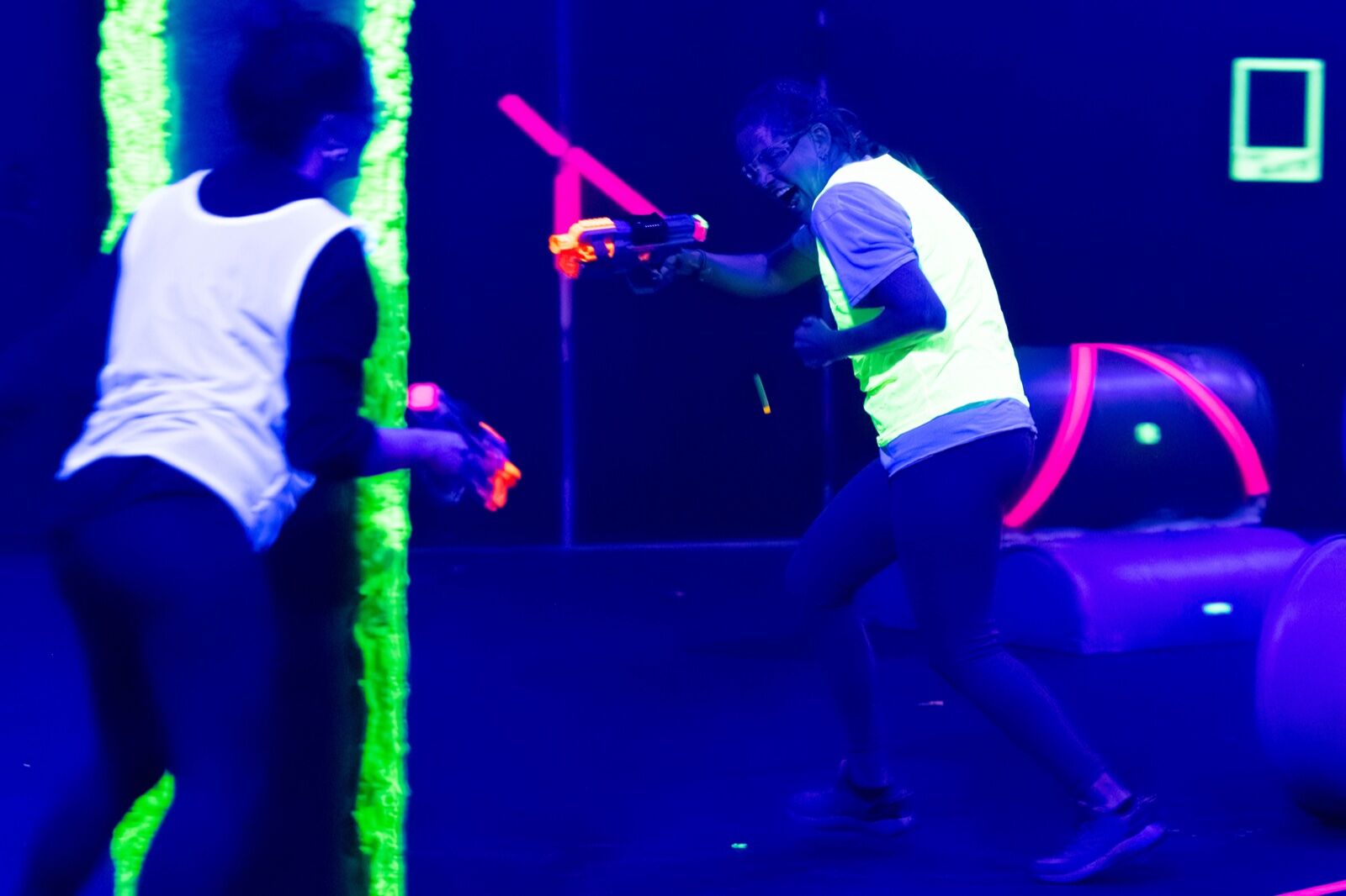 Two players firing foam blasters at close range across a glowing pillar in the dark arena