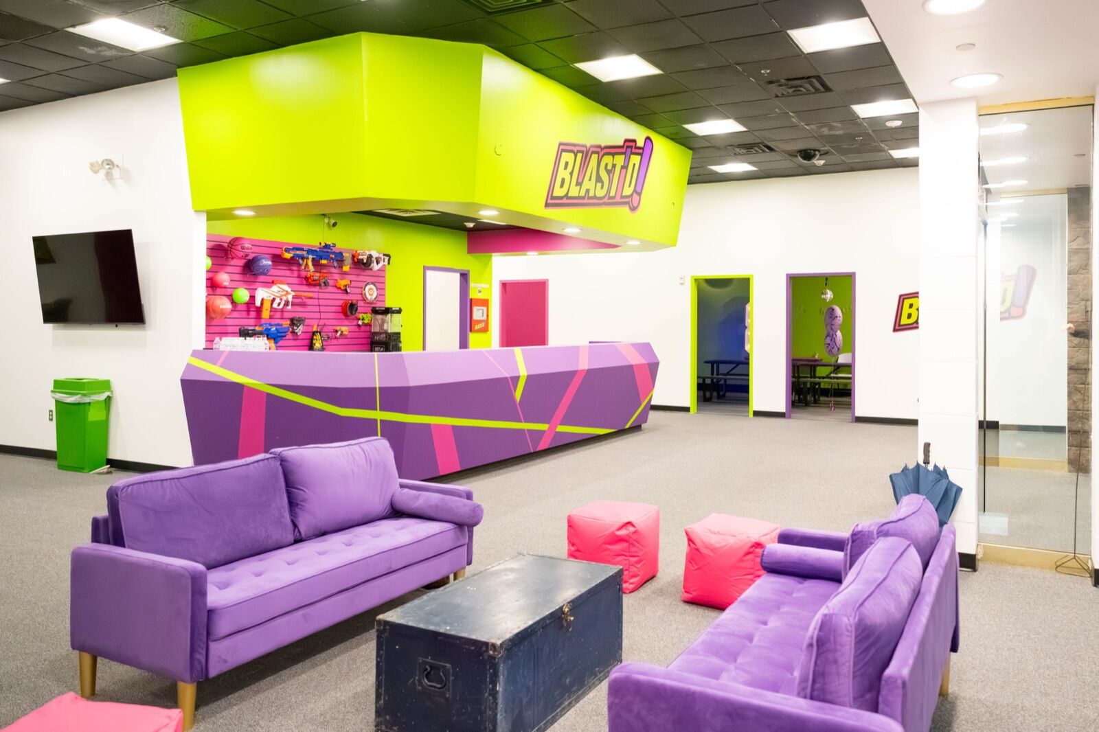 The Blast'D! Arena lobby — the front desk under the logo, a wall of foam blasters, and purple lounge seating