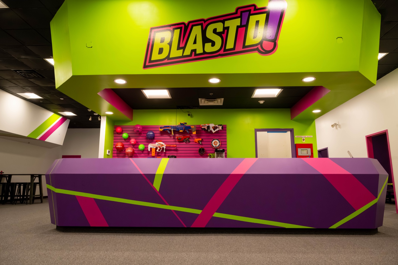 The Blast'D! front desk beneath the illuminated logo, with a wall of foam blasters and balls behind it